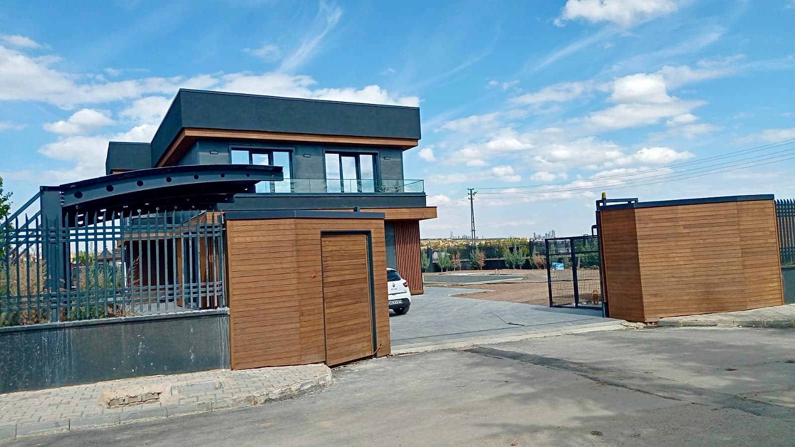 Entrance gate with curved metal canopy, timber guard booth, and driveway