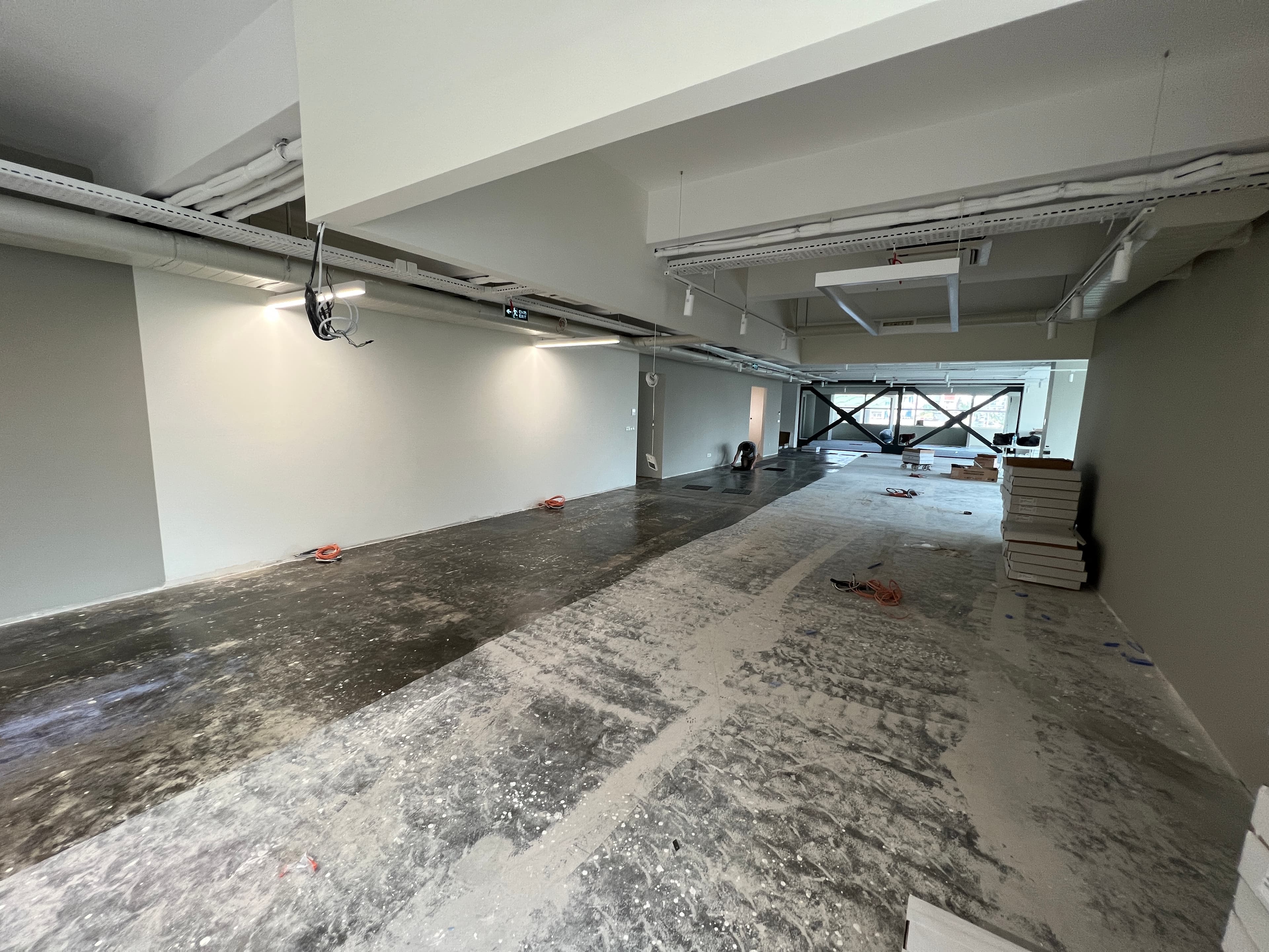 Long construction view with raw concrete floor and exposed ceiling conduits