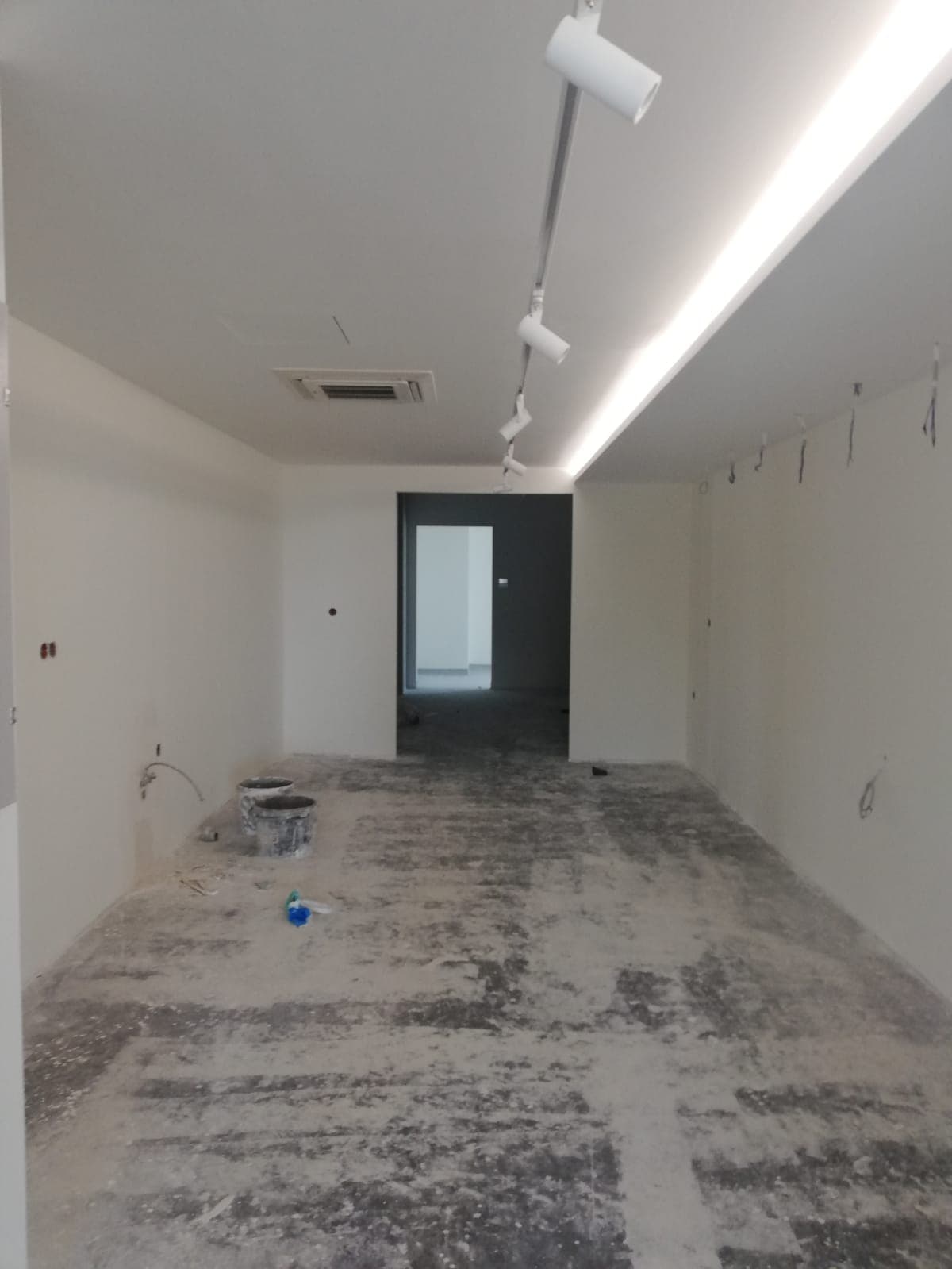 Narrow room under construction with track lighting and raw concrete floor